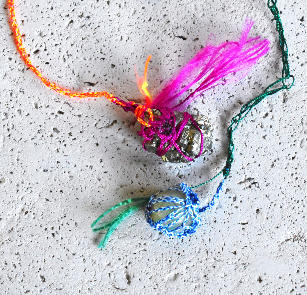 Close-up of raw pyrite and nephritic jade pendants wrapped in neon hand-crocheted paracord